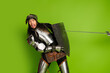 © deagreez - Young man in medieval knight armor with shield and sword on bright green background showcasing historical theme and humor