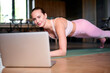 © khmelev - woman doing plank exercise while engaging with laptop for online fitness class at home. focus on healthy lifestyle and digital training. yoga mat on wooden floor.