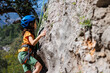 © zhukovvvlad - boy climber in a helmet. A determined and strong boy climber climbs a steep mountain wall. A child overcomes a difficult route.