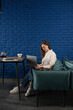 © ADDICTIVE STOCK - Woman Working on Laptop in Cozy Blue Cafe with Tea