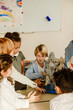 © Drobot Dean - A diverse group of first-grade students gathered around a spinning metal wheel instrument in their first-grade classroom, with a blond White boy sitting near it and looking at them