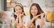 © PixLOG - Closeup portrait of Two cheerful Asian women smiling warmly at the camera with beauty products arranged in front of them in a cozy home. happy female friendship, lifestyle, and influencer concept.