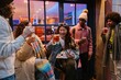 © Drobot Dean - A 25-year-old Asian woman with her dachshund dog in her lap, drinking and laughing together with a group of her friends as they relax outside of a bar on a city street in the evening