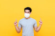 © Atstock Productions - Young Asian man wearing face mask with hands pointing up to copy space on isolated yellow background studio shot