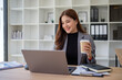 © wattana - Smiling businesswoman enjoying coffee while working on laptop in modern office.