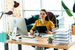 © deagreez - Confident businesswoman sitting at desk in bright modern office, holding clipboard for daily tasks and workplace management