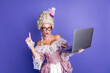 © deagreez - Elegant woman dressed as an aristocratic queen with a laptop on a unique purple background showcasing mix of history and technology