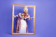 © deagreez - Elegant woman in a vintage royal costume posing with decorative frame against a vibrant purple backdrop