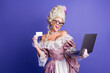© deagreez - Woman Wearing Historical Dress Holding a Credit Card and a Laptop Against a Purple Background