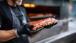 © OleksandrZastrozhnov - A man is holding a large piece of meat, possibly a rack of ribs, in his gloved hands