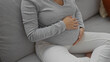 © Krakenimages.com - Pregnant woman in casual home setting touching belly in living room indicating peaceful and expectant atmosphere with subtle natural lighting showcasing comfortable lifestyle