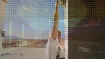 Poster - female worker handling open electrical cabinet at wind farm, showing animated finance graphs
