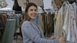 © Krakenimages.com - Woman shopping in a street market, examining clothes on a rack, smiling in a casual grey sweater, enjoying the outdoor shop setting and selecting items.