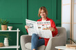 © Pixel-Shot - Pretty young woman with newspaper sitting on armchair at home