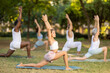 © JackF - Yoga female coach conduct rehearsal for multinational followers in park, leading of performing exercises, do fulfil warrior pose. People practice sport during yoga workout in nature