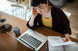 © Geber86 - Stressed Asian woman managing personal finances at kitchen counter with laptop and paperwork
