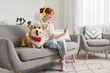 © Pixel-Shot - Teenage redhead girl and cute Corgi dog with headphones using mobile phone on sofa at home