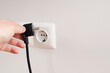 © Trik - Man putting on or removing electric plug cable in socket, closeup. Electrical equipment wires and power strips on the wall