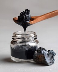 Poster - Close up of shiny black substance dripping from wooden spoon into glass jar on gray surface