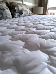 Poster - Comfortable white quilted mattress pad with soft pillows on a cozy bed in a bright bedroom for restful sleep and relaxation in a modern home