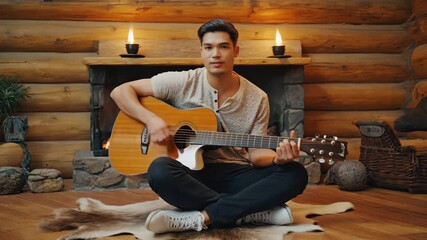 Poster - Man playing acoustic guitar by fireplace in log cabin.