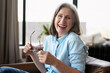 © Maria Vitkovska - Happy senior woman laughing holding eyeglasses sitting on sofa at home