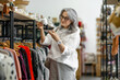 © Валентина Хруслова - A woman with grey hair looks at vintage tableware in a boutique