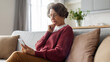 © Home-stock - Thoughtful senior woman sitting on couch at home and looking at cellphone, reading news or learning to use modern technologies, panorama shot