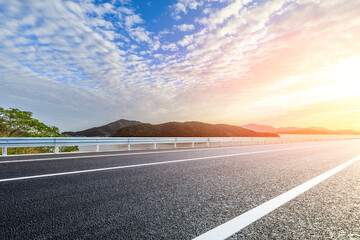 Wall Mural - asphalt road and lake with mountain scenery at sunset
