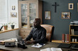 © AnnaStills - Wide shot of spacious office with African American pastor working on laptop sitting at wooden table