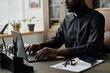 © AnnaStills - Medium shot of African American pastor typing on laptops keyboard while sitting at table with rosary, bible and office supplies on top