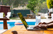 © didar - work from home concept, young man works on computer in the garden of his house with pool, writes email