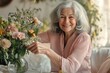 © IRINA - An elderly woman with beautifully styled gray hair is sitting on a white sofa and arranging flowers in a vase on the table. Daytime. Bright soft lighting.
