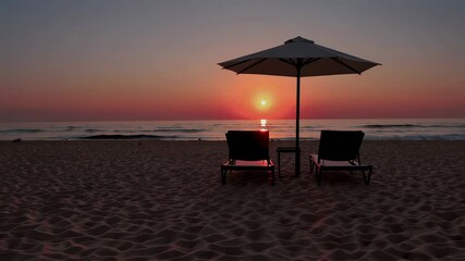 Poster - Golden sunrise casting warm light across tranquil ocean, gently lapping waves caressing sandy shoreline with inviting sunbeds and umbrella beneath vibrant, colorful morning sky