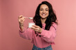 © Nataliya - Smiling pleased dark-haired young lady eating an appetizing dairy product in front of the camera on the pink background. Healthy food concept