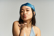 © LIGHTFIELD STUDIOS - Joyful young woman blowing kisses with a playful smile against a neutral background