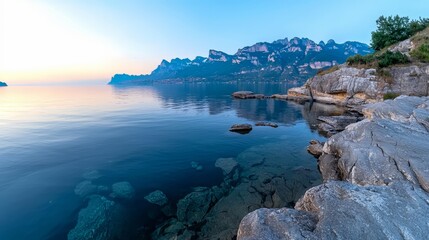 Poster - Beautiful view of the ocean with a rocky shoreline. The water is calm and the sky is a mix of blue and orange. The scene is serene and peaceful