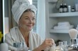 © Deris Firmansyah - Gorgeous mid age older adult 50 years old blonde woman wears bathrobe in bathroom applying nourishing antiage face skin care cream treatment, looking at mirror doing daily morning beauty routine.