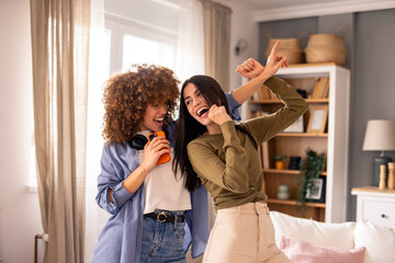 joyful female friends dancing and celebrating in bright living room with casual modern home interior