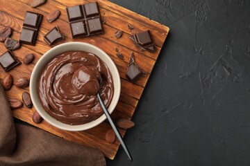Wall Mural - tasty pudding in bowl, pieces of chocolate and cocoa beans on black table, flat lay. space for text
