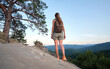 © bilanol - Hiker woman standing on mountain footpath enjoying nature during her travel on wilderness trail. Lonely female traveler traversing high hilltop route. Healthy lifestyle concept