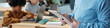 © pressmaster - Image showing teacher holding tablet while conducting lesson for students in classroom. Several students are seen working on laptops in background creating collaborative learning environment
