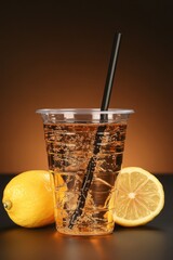 Poster - Refreshing lemon drink with bubbles in a plastic cup with straw and lemon halves on a dark surface against a gradient brown background studio shot