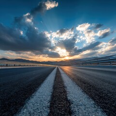 Poster - Asphalt road under dramatic sky with sun rays and clouds leading to distant mountains at sunset creating a sense of travel freedom and scenic landscape