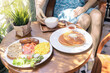 © Vladimir Razgulyaev - Breakfast spread featuring pancakes, eggs, and sausage served with coffee at a cozy cafe in the morning. A woman in the background is drinking coffee