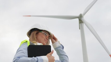 Poster - A female engineer, equipped with safety gear and a clipboard, evaluates a wind turbine on a cloudy day, highlighting advancements in renewable energy crucial for a sustainable future