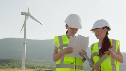 Fototapete - Two engineers in safety gear are onsite at a wind farm, reviewing plans and collaborating to advance sustainable technology and innovative green energy solutions for a cleaner future