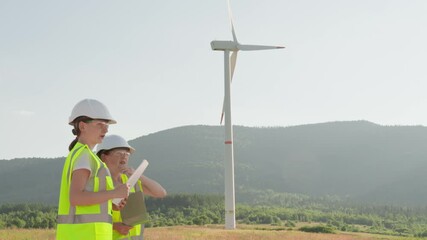 Poster - Two enthusiastic girls in vibrant safety gear explore a towering wind turbine against a scenic backdrop, symbolizing ecofriendly energy and a promising future in engineering innovations