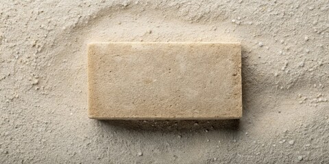 Poster - A textured beige block rests on a bed of fine, light-colored sand, creating a simple yet elegant composition.