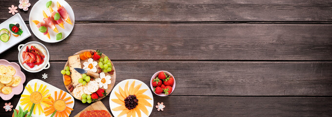 Aufkleber - Summer garden party food corner border. Assortment of fun flower theme charcuterie items, cheese, fruit, vegetables and finger snacks. Above view on a dark wood banner background.